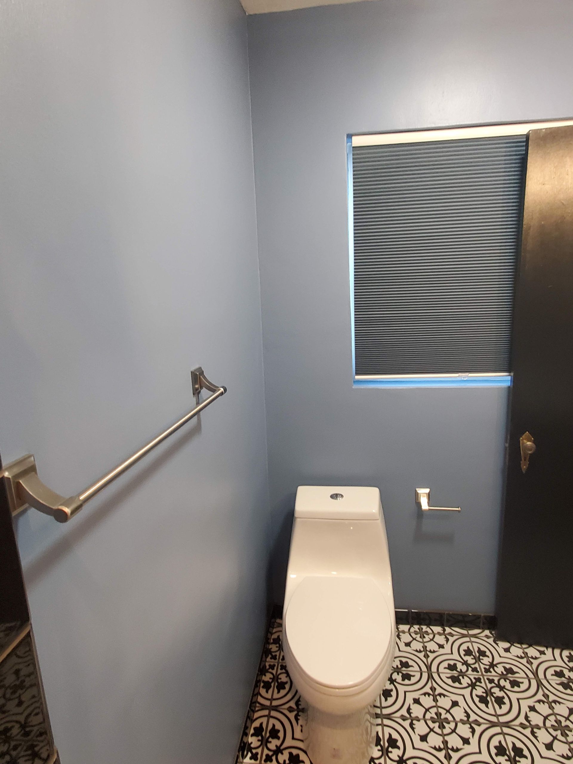 A toilet is sitting in a bathroom next to a window.