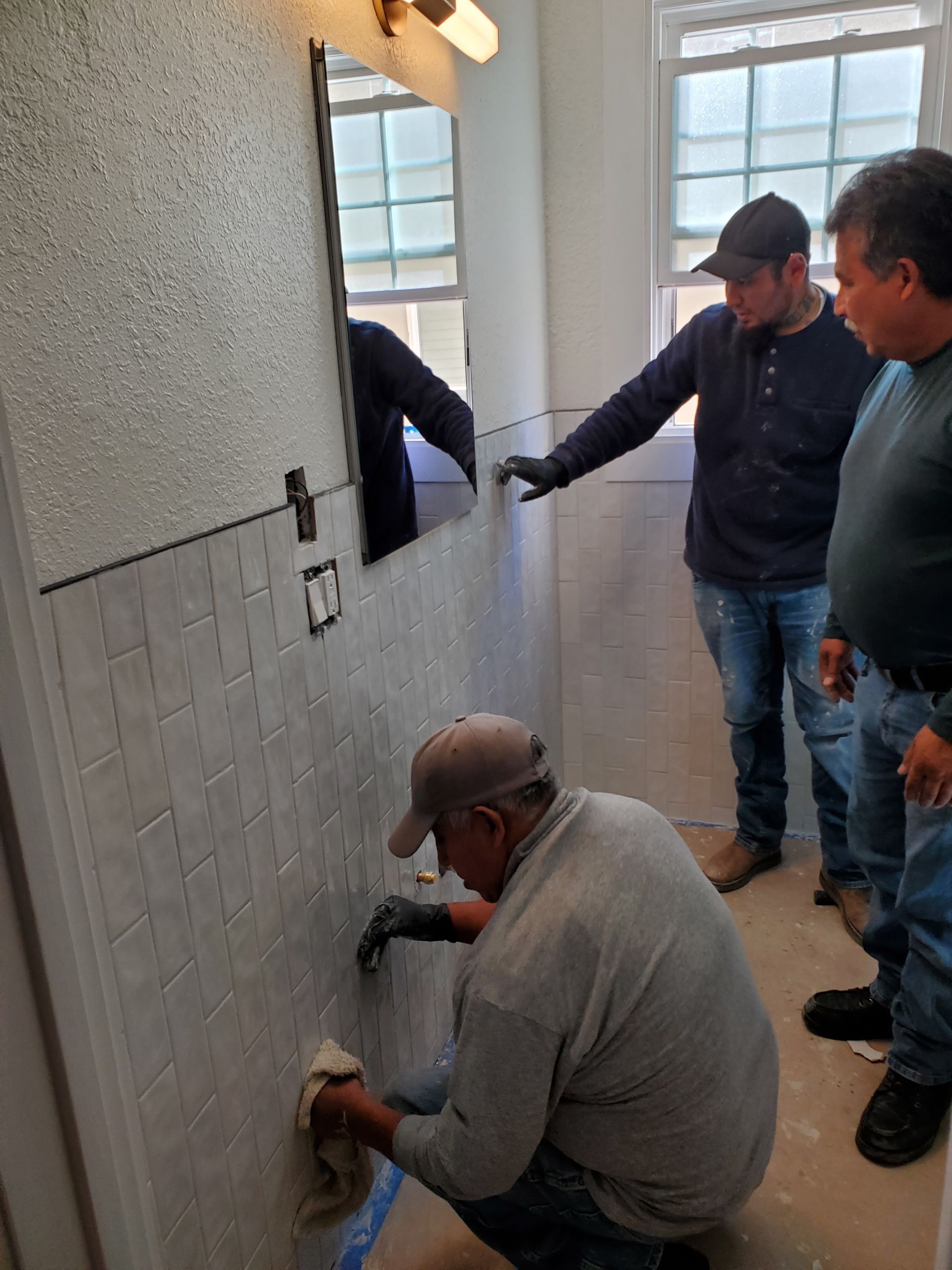 A group of men are working on a bathroom wall