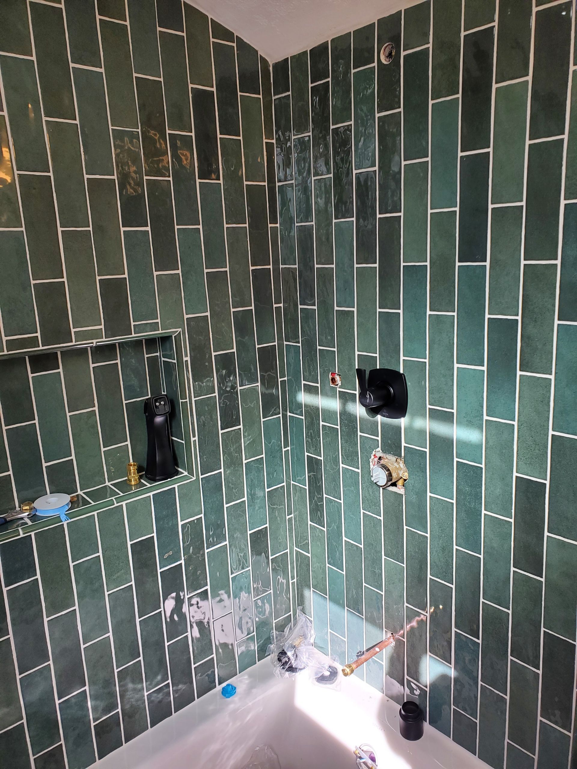 A bathroom with green tiles and a bathtub.