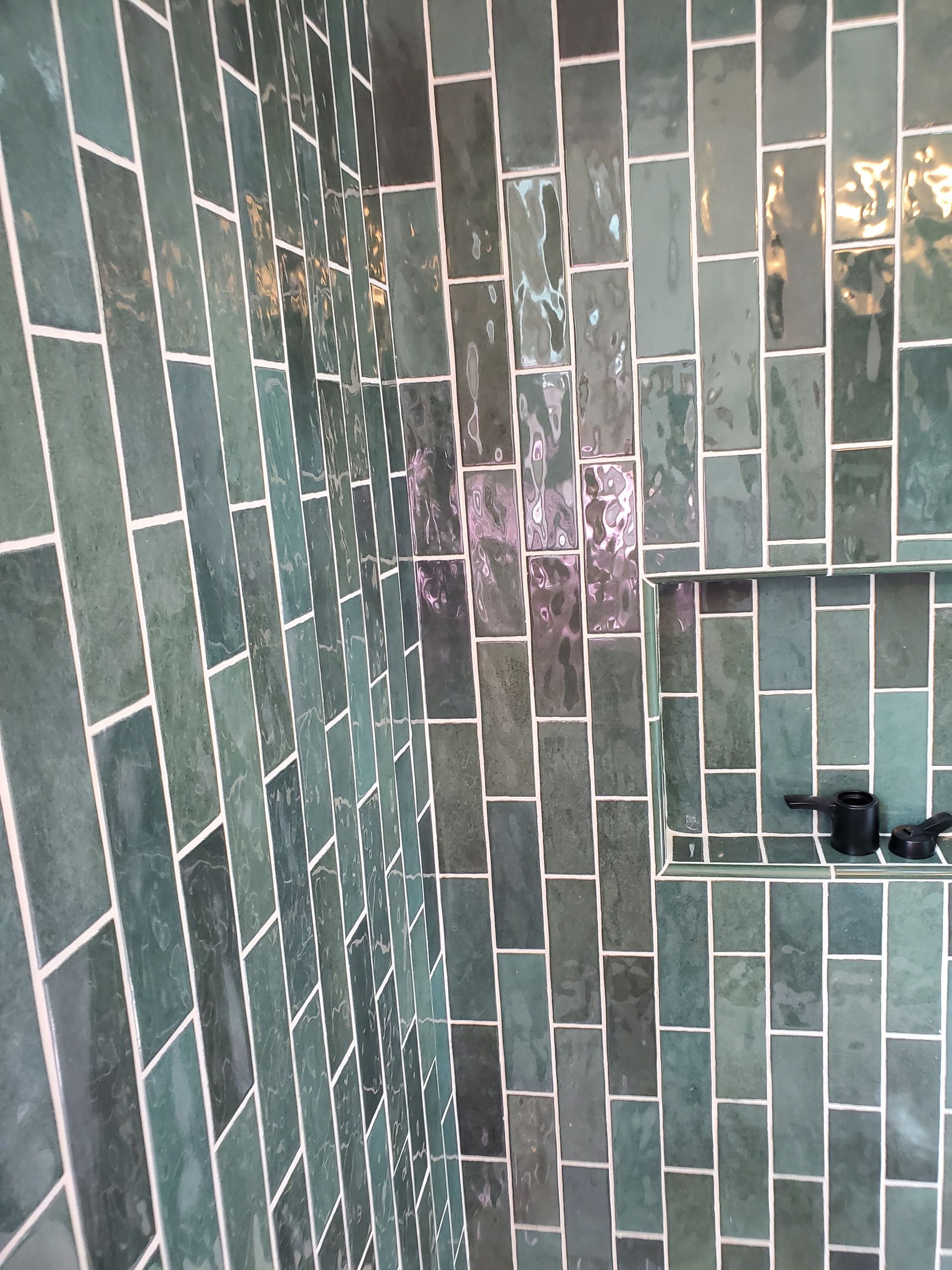 A close up of a shower with green tiles on the wall and floor.