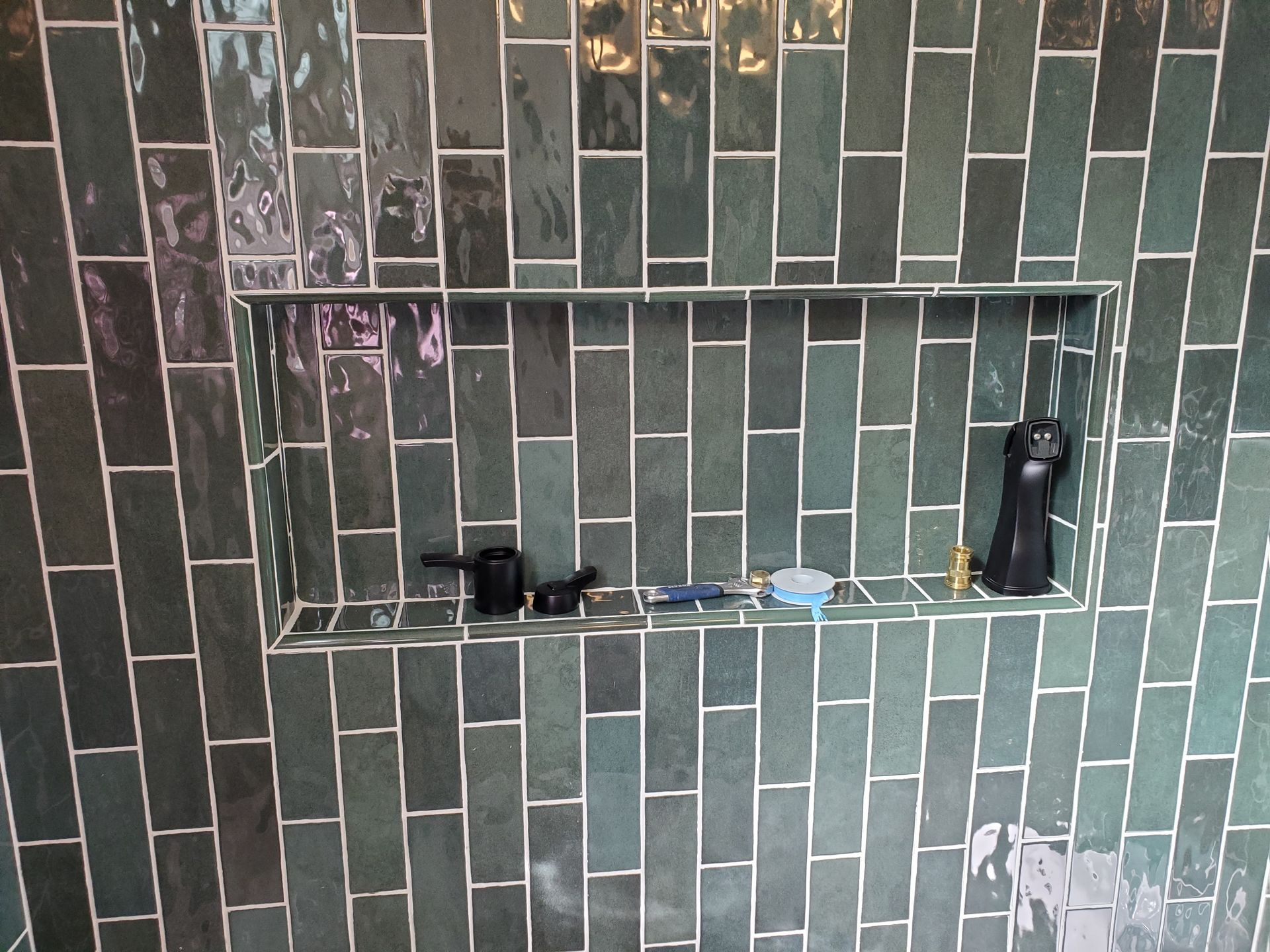 A bathroom with green tiles and a shelf in the shower