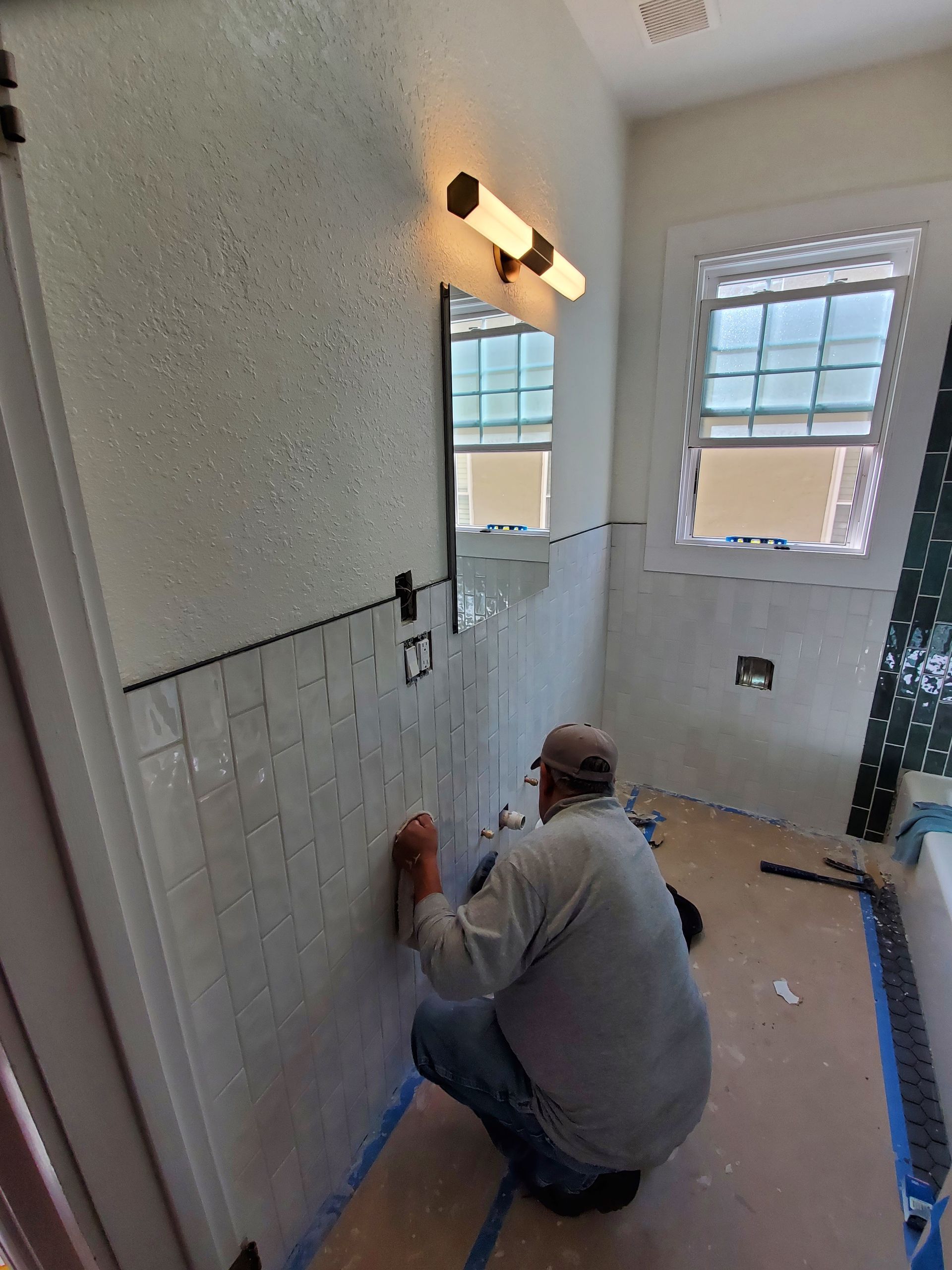 A man is kneeling down in a bathroom cleaning a wall.