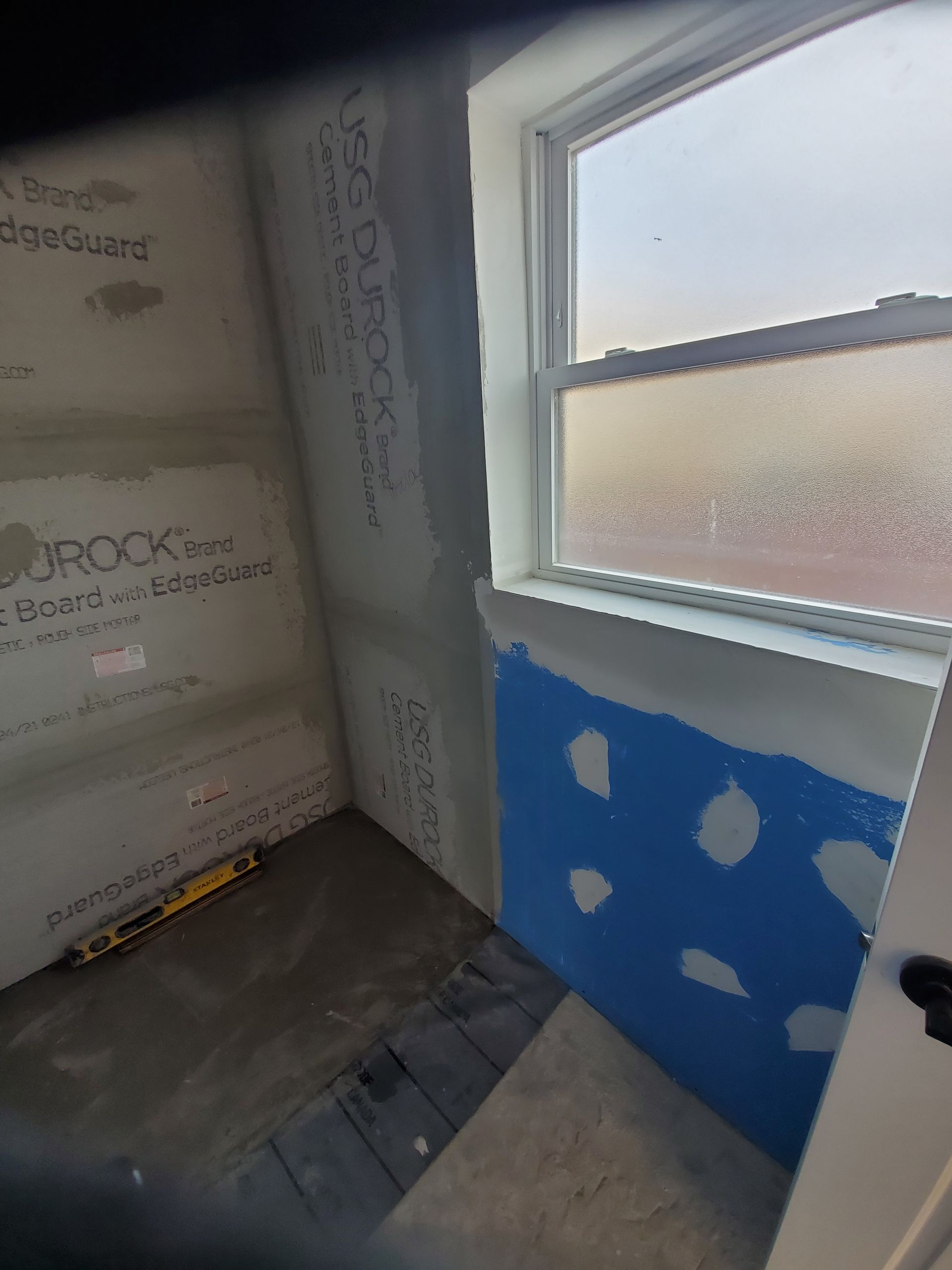 A bathroom under construction with a window and a blue wall.