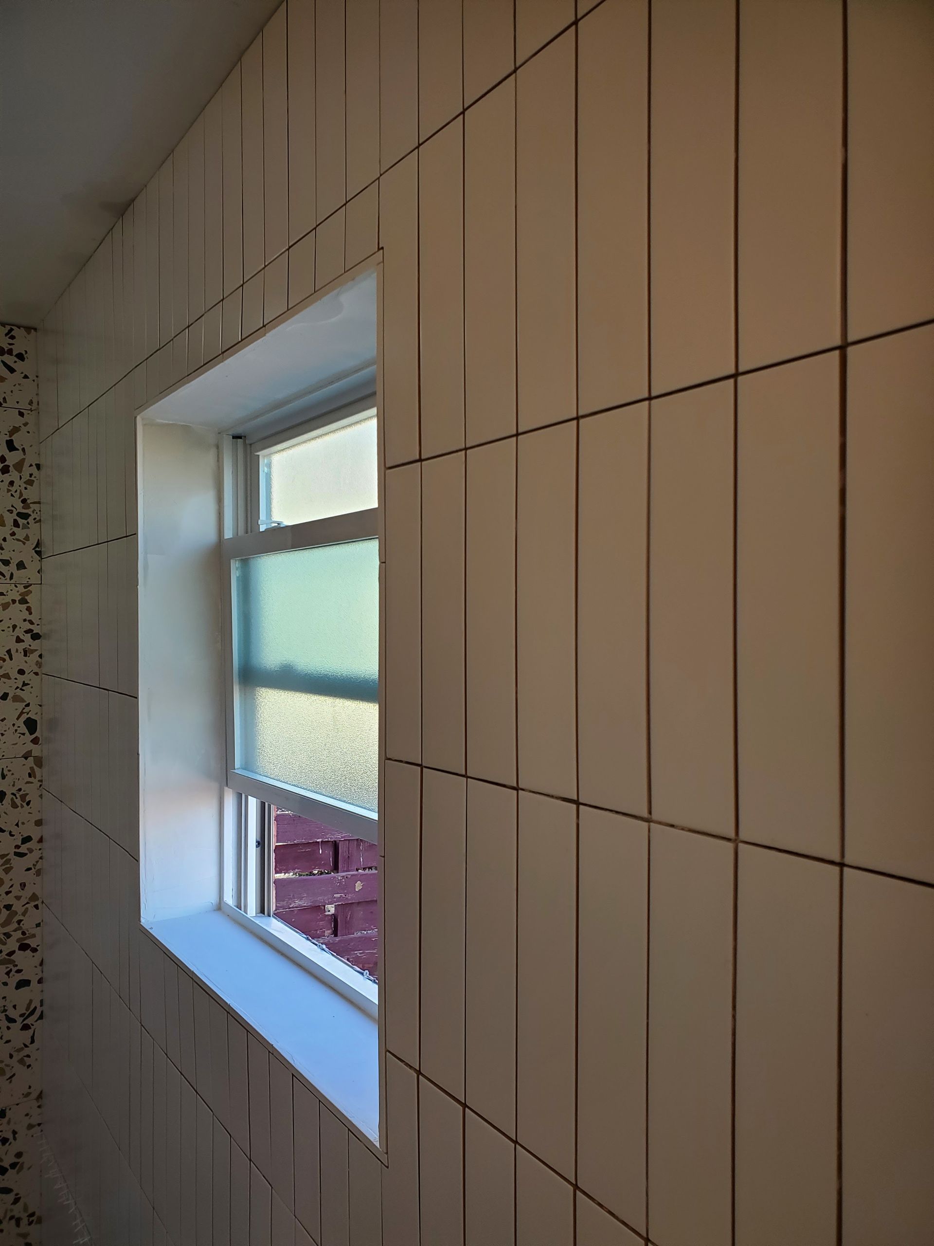 A white tiled wall with a window in it