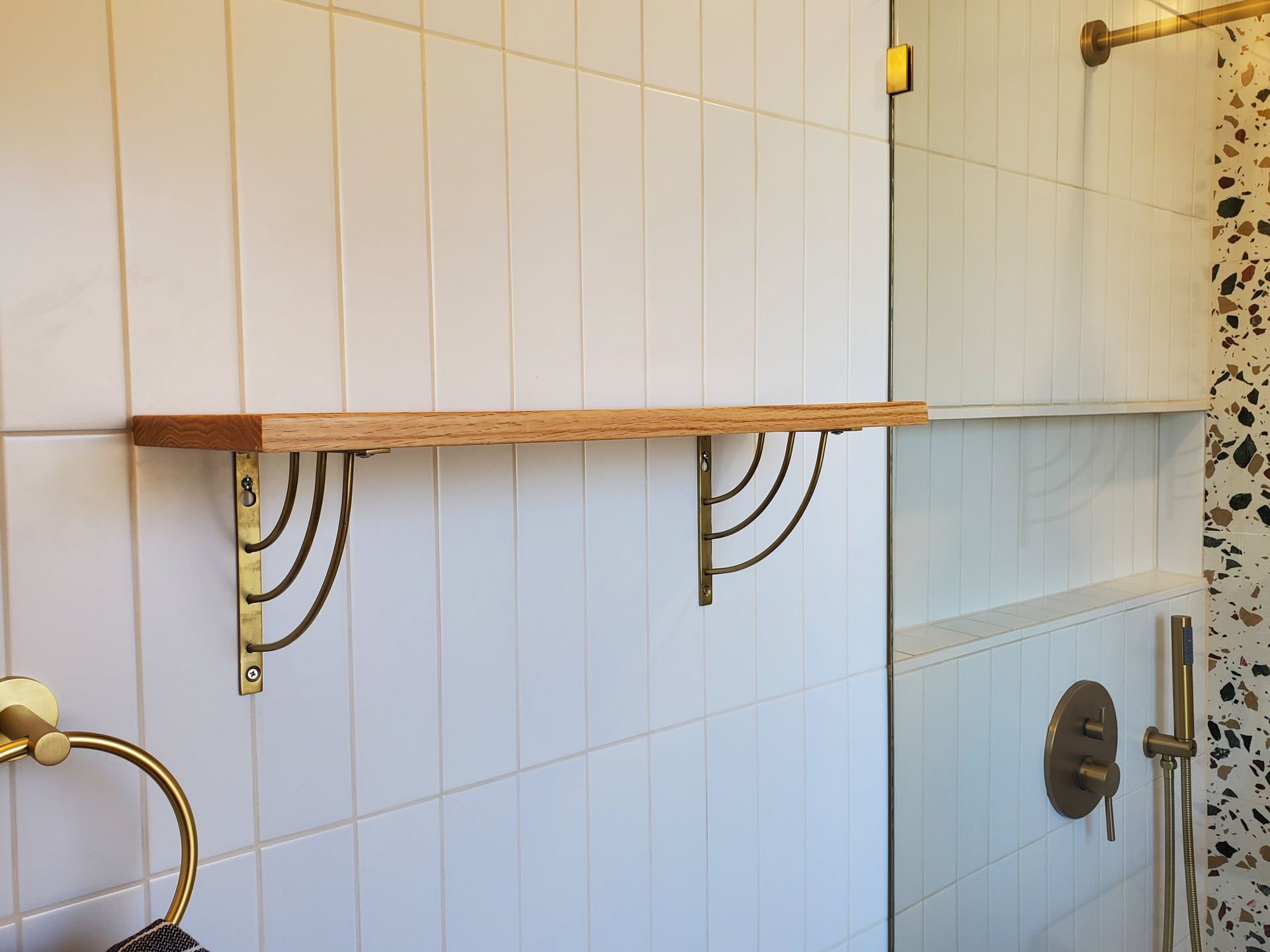 A bathroom with a wooden shelf and brass brackets