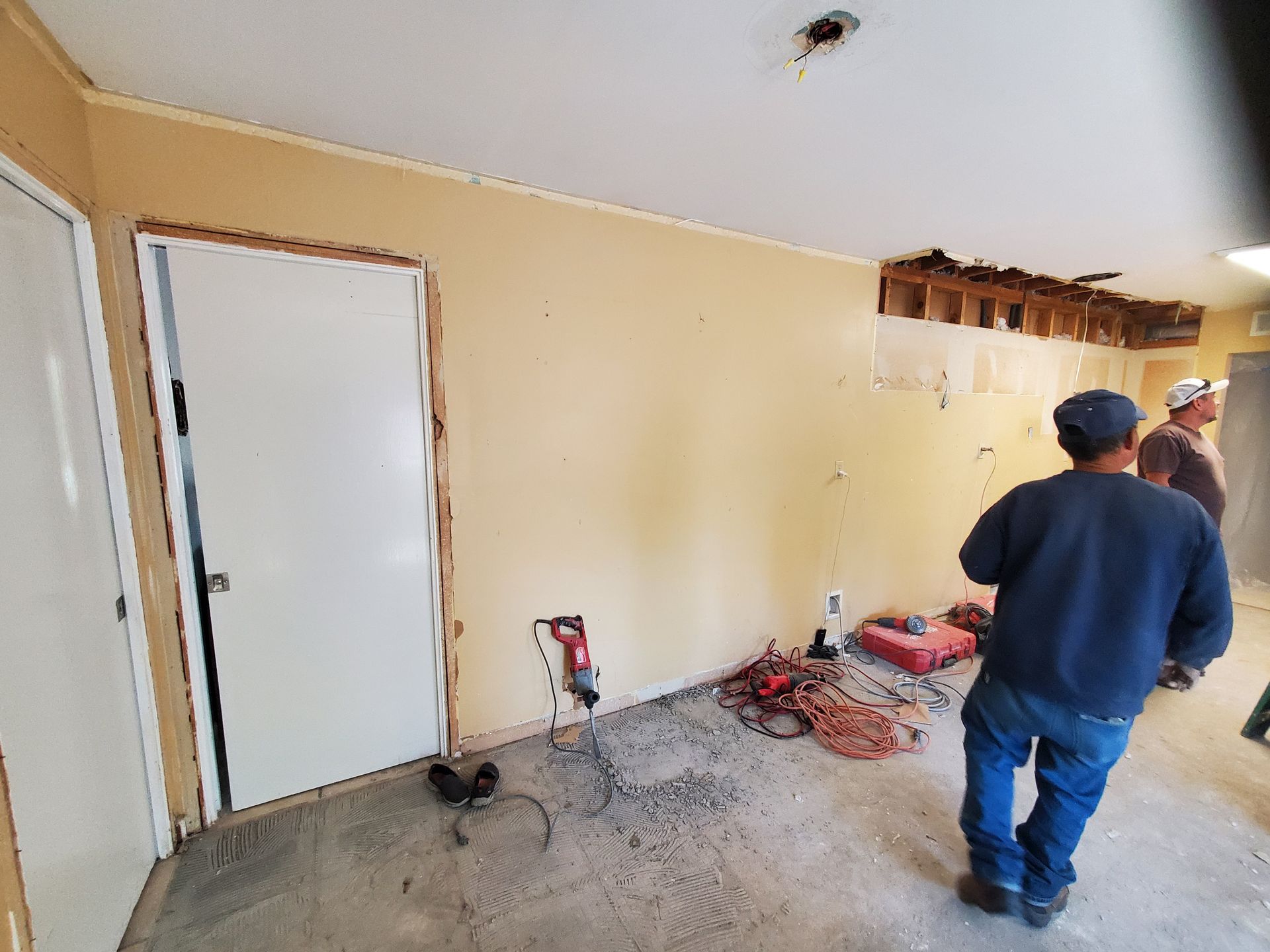 Two men are standing in a room with a hole in the ceiling.