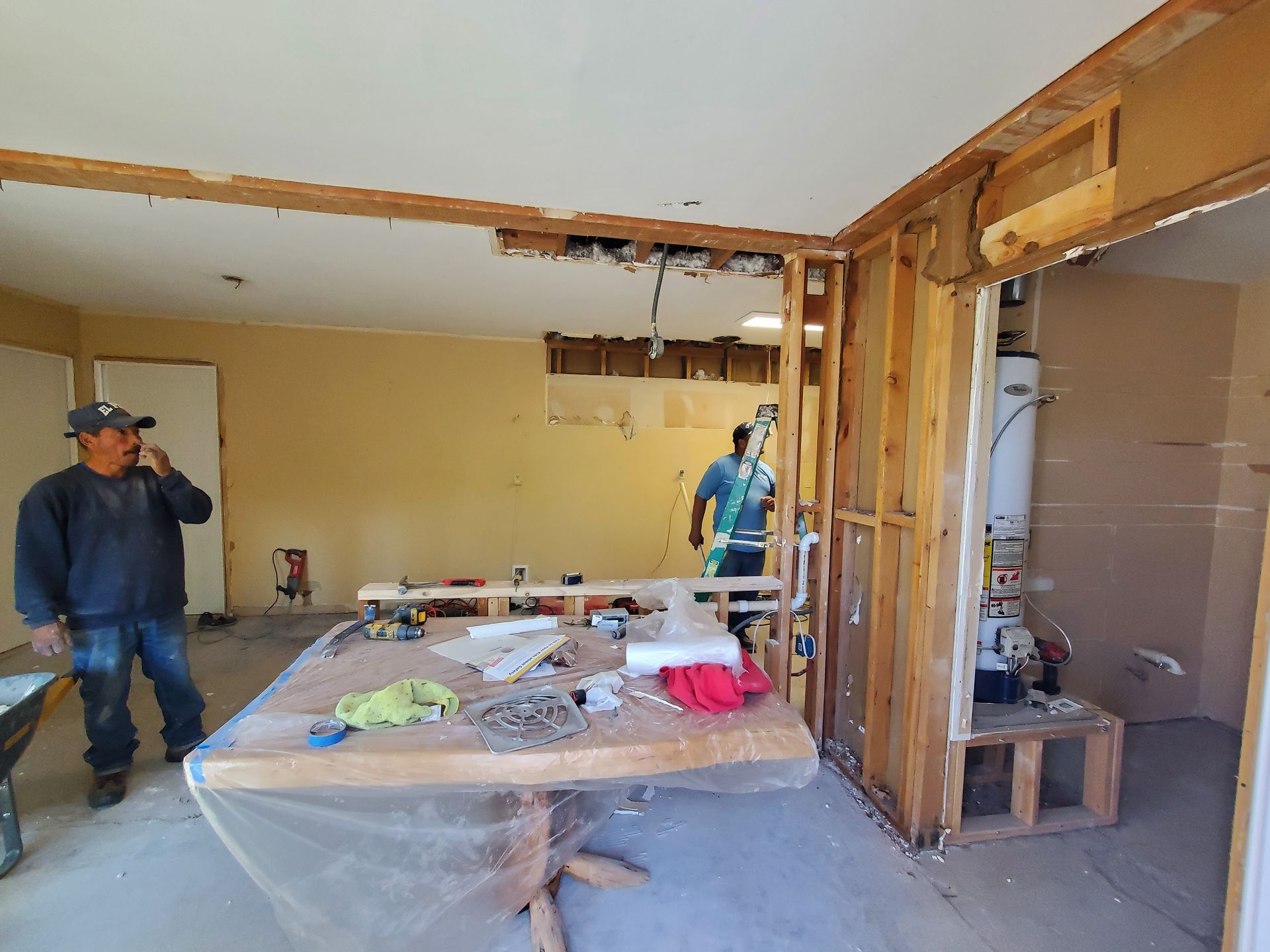 A man is standing in a room with a table and talking on a cell phone.