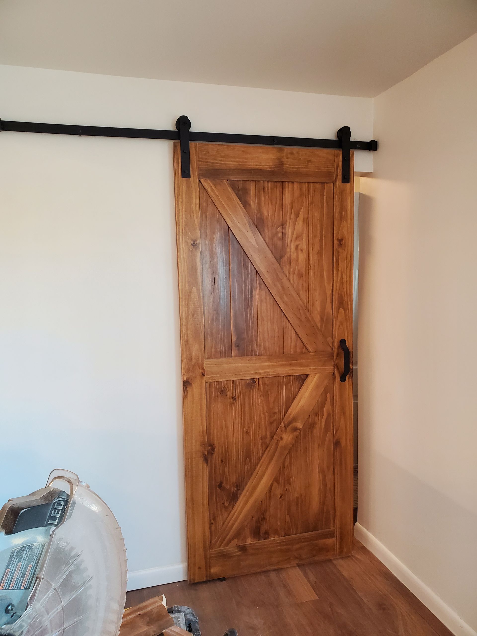 A wooden sliding barn door is hanging on a white wall in a room.