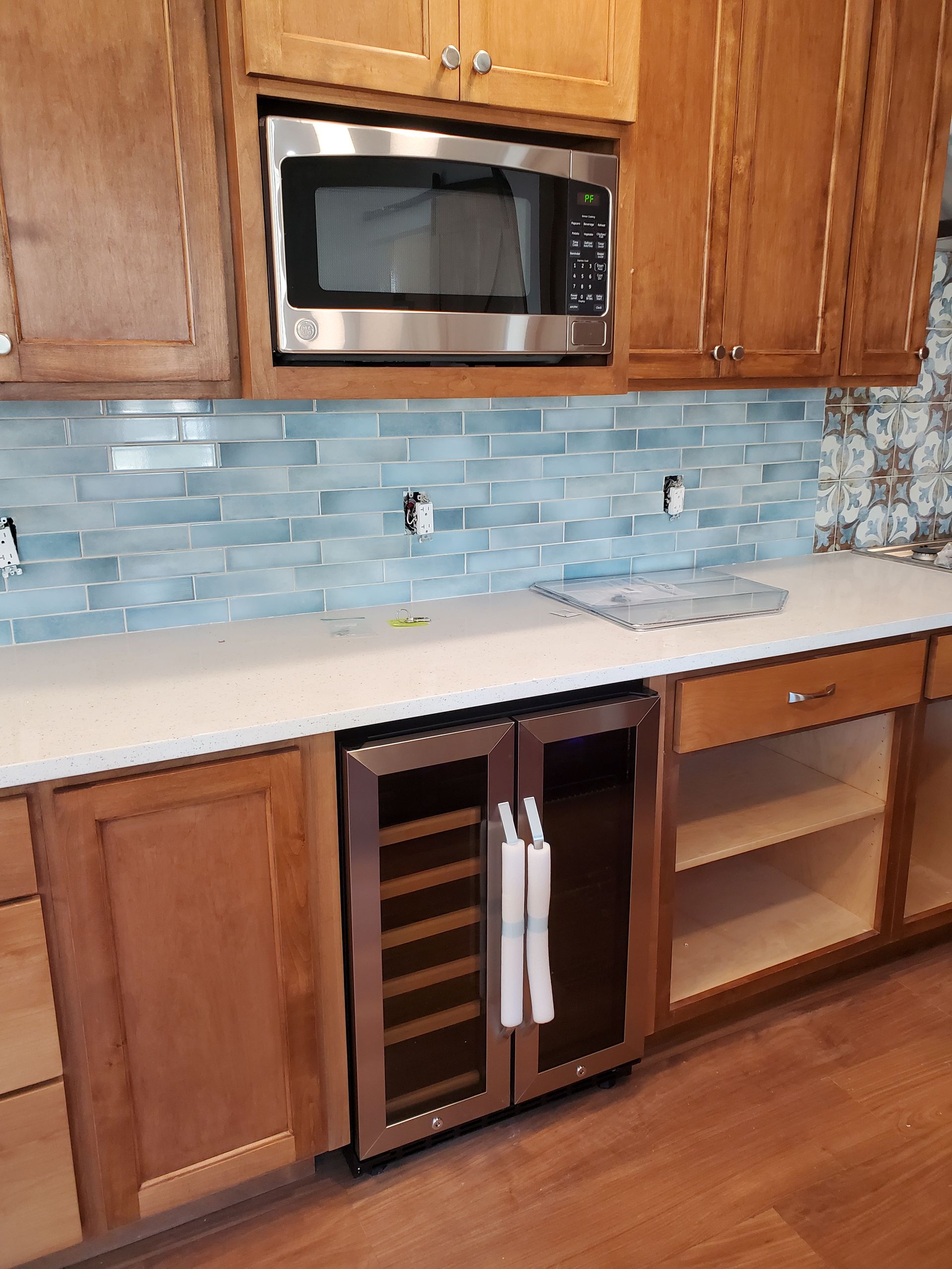 A kitchen with wooden cabinets , stainless steel appliances , a wine cooler and a microwave.