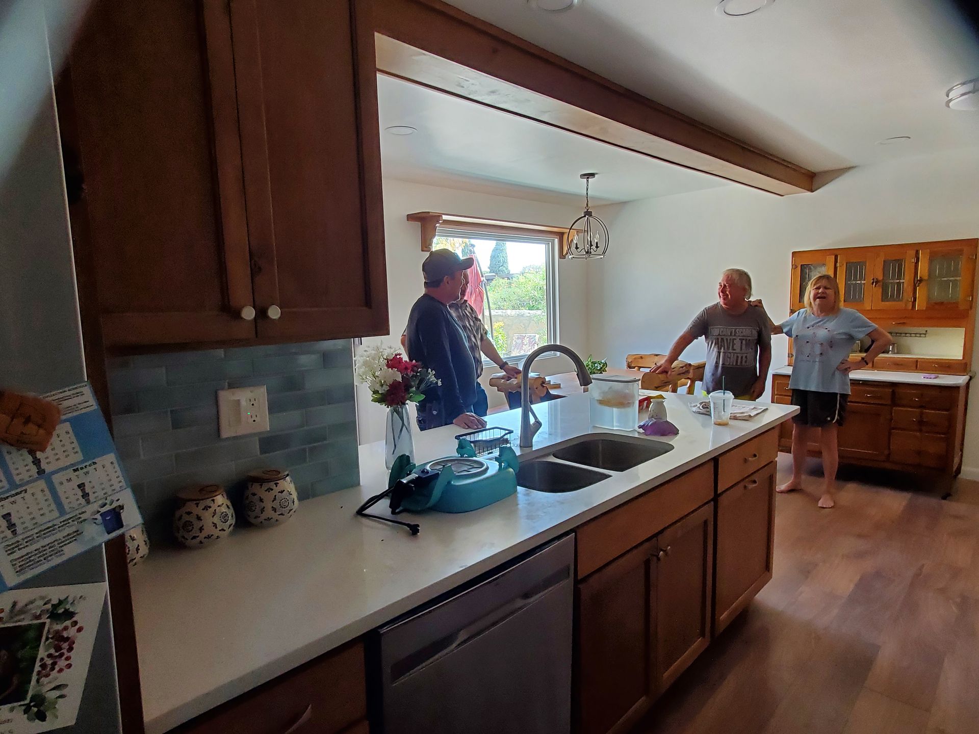 A group of people are standing in a kitchen next to a sink.