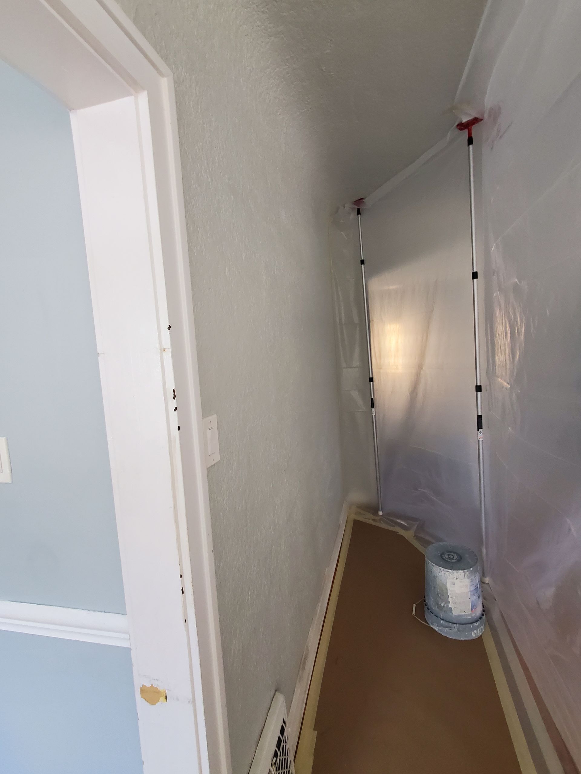 A hallway with a plastic sheet on the wall and a roll of tape on the floor.