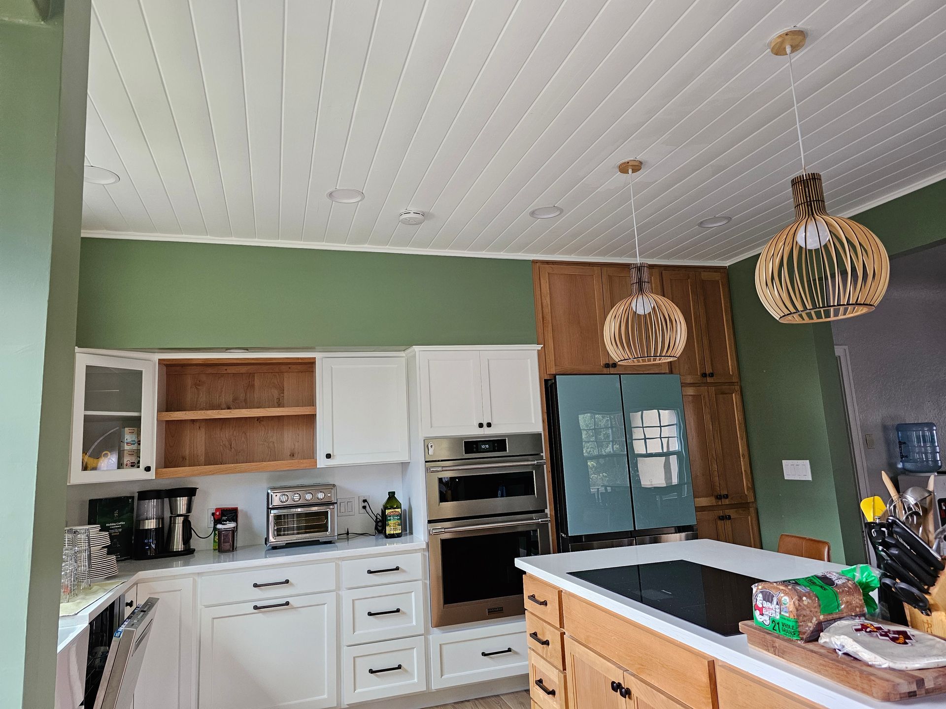 A kitchen with white cabinets , wooden cabinets , a refrigerator , and a stove top oven.