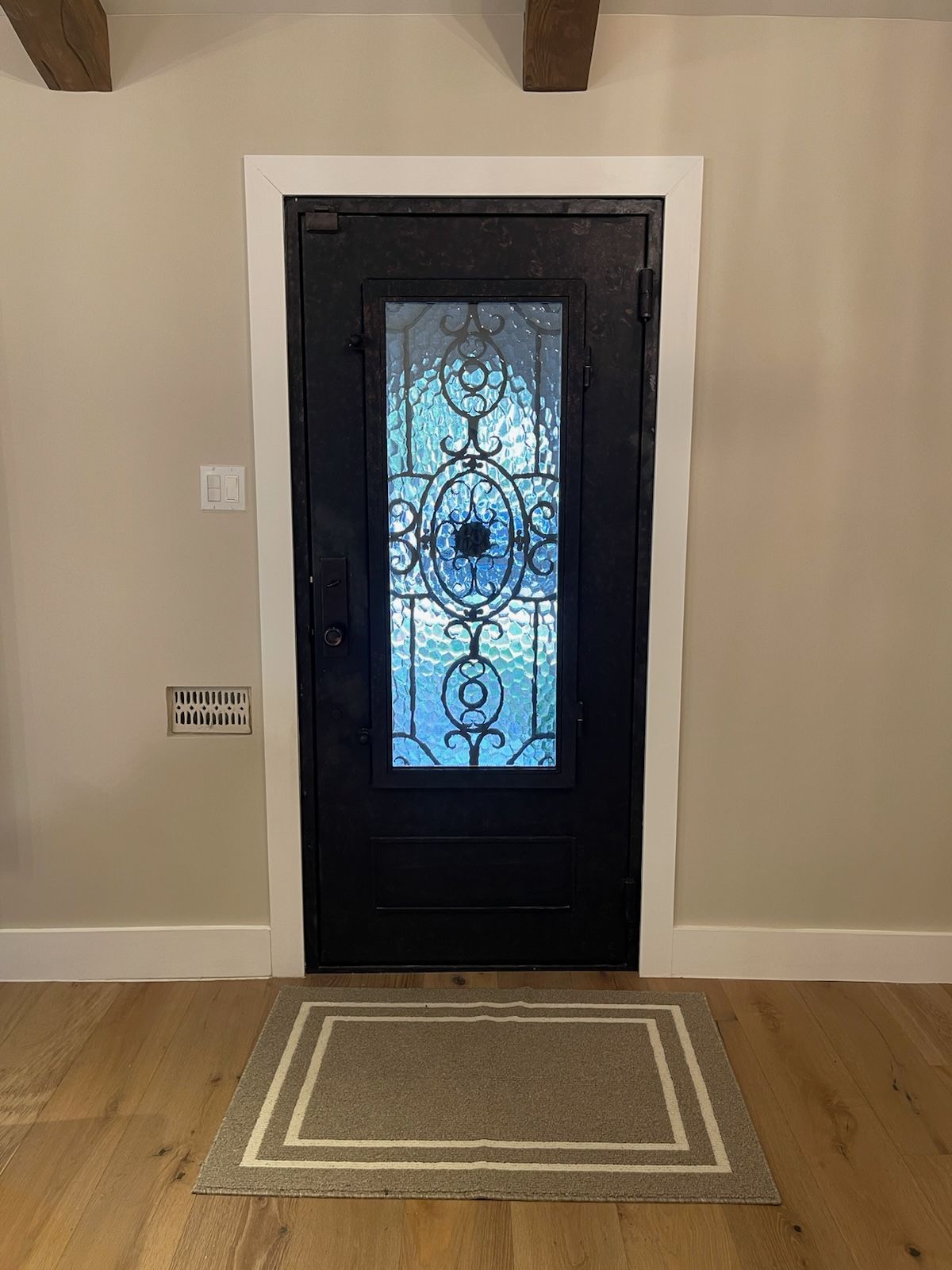 A black door with a stained glass window and a rug in front of it.