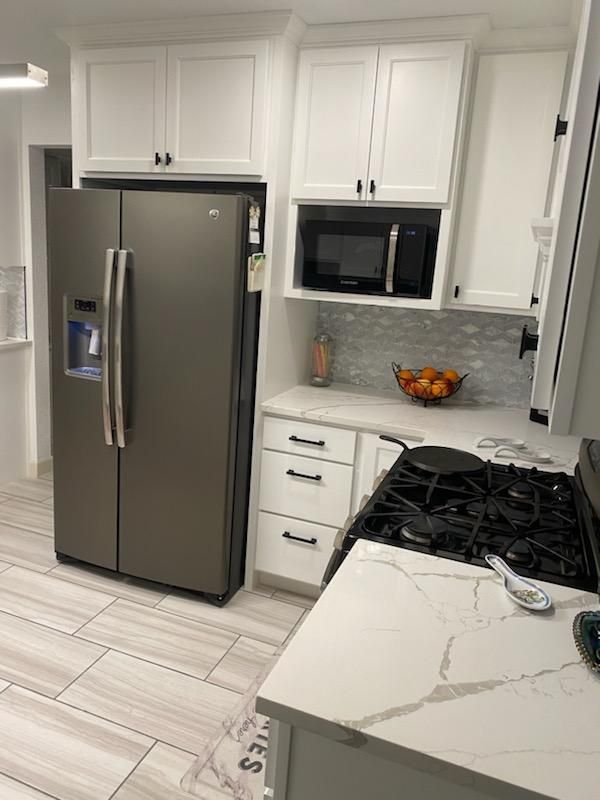 A kitchen with white cabinets , a stove , a refrigerator , and a microwave.