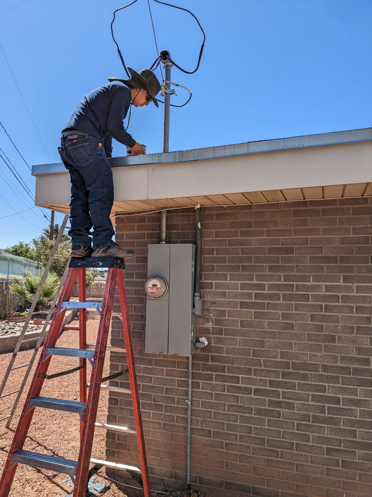 A man is standing on a ladder working on a roof.