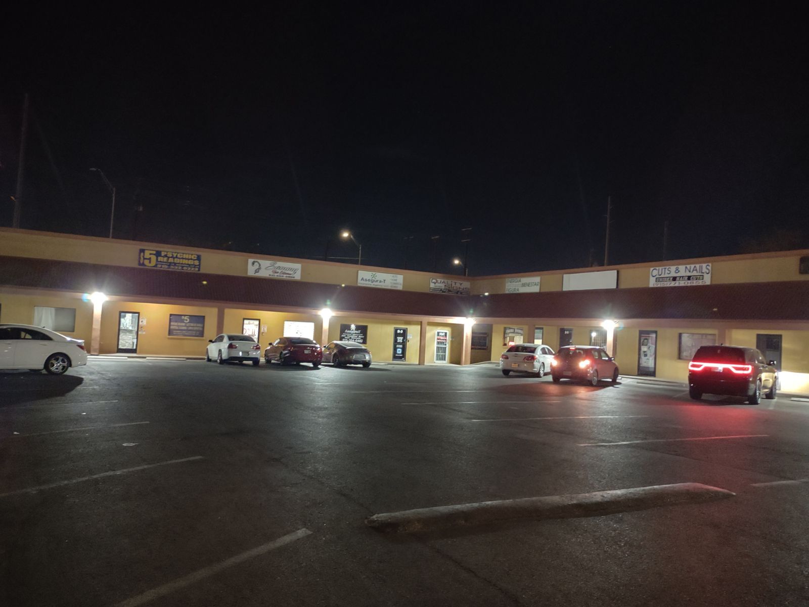 A parking lot with cars parked in front of a building at night