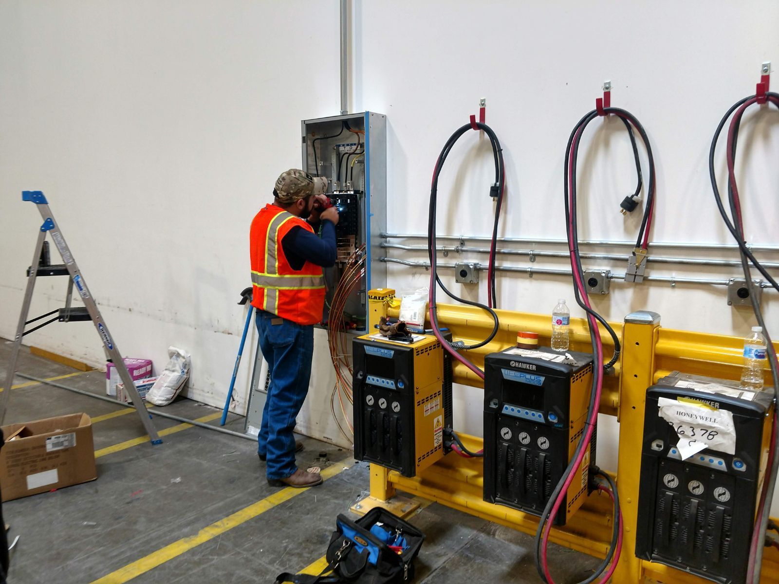 A man is working on an electrical box in a warehouse.