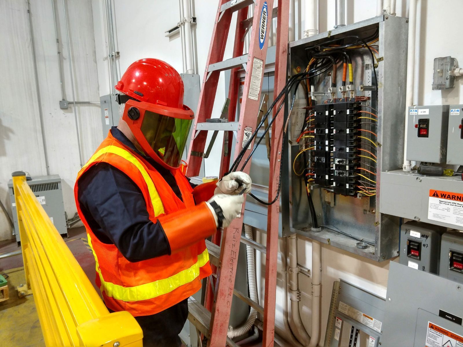 A man wearing a helmet and safety vest is working on an electrical box.