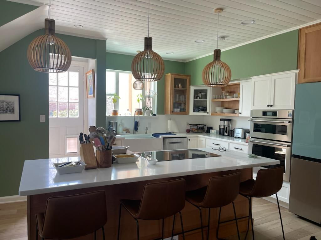 A kitchen with green walls , white cabinets , stainless steel appliances and a large island.