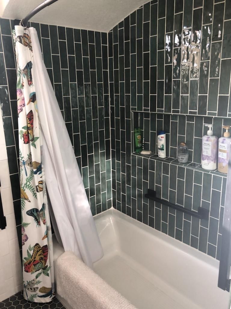 A bathroom with green tiles and a bathtub with a shower curtain hanging over it.