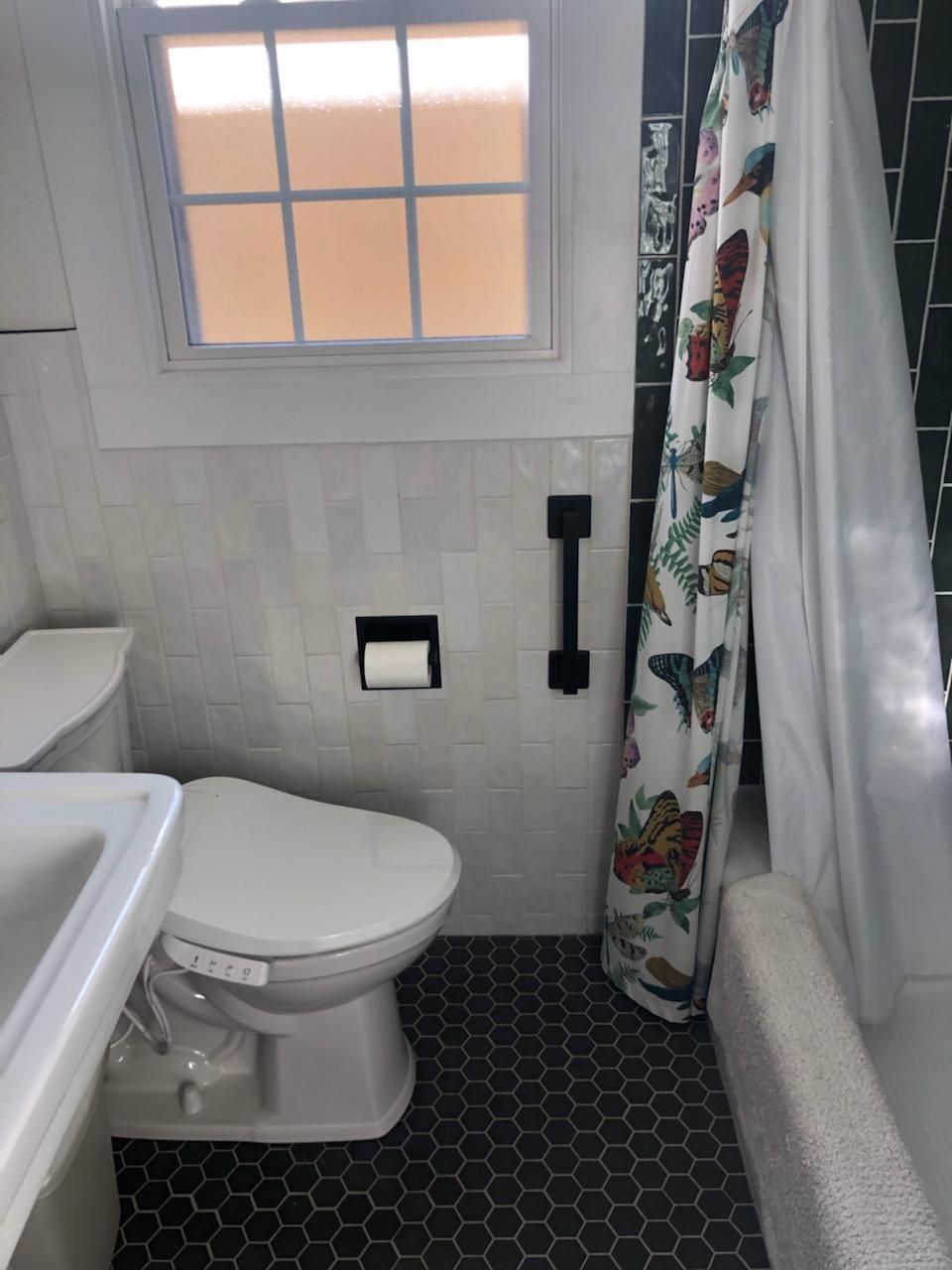 A bathroom with a toilet , sink , shower curtain and window.