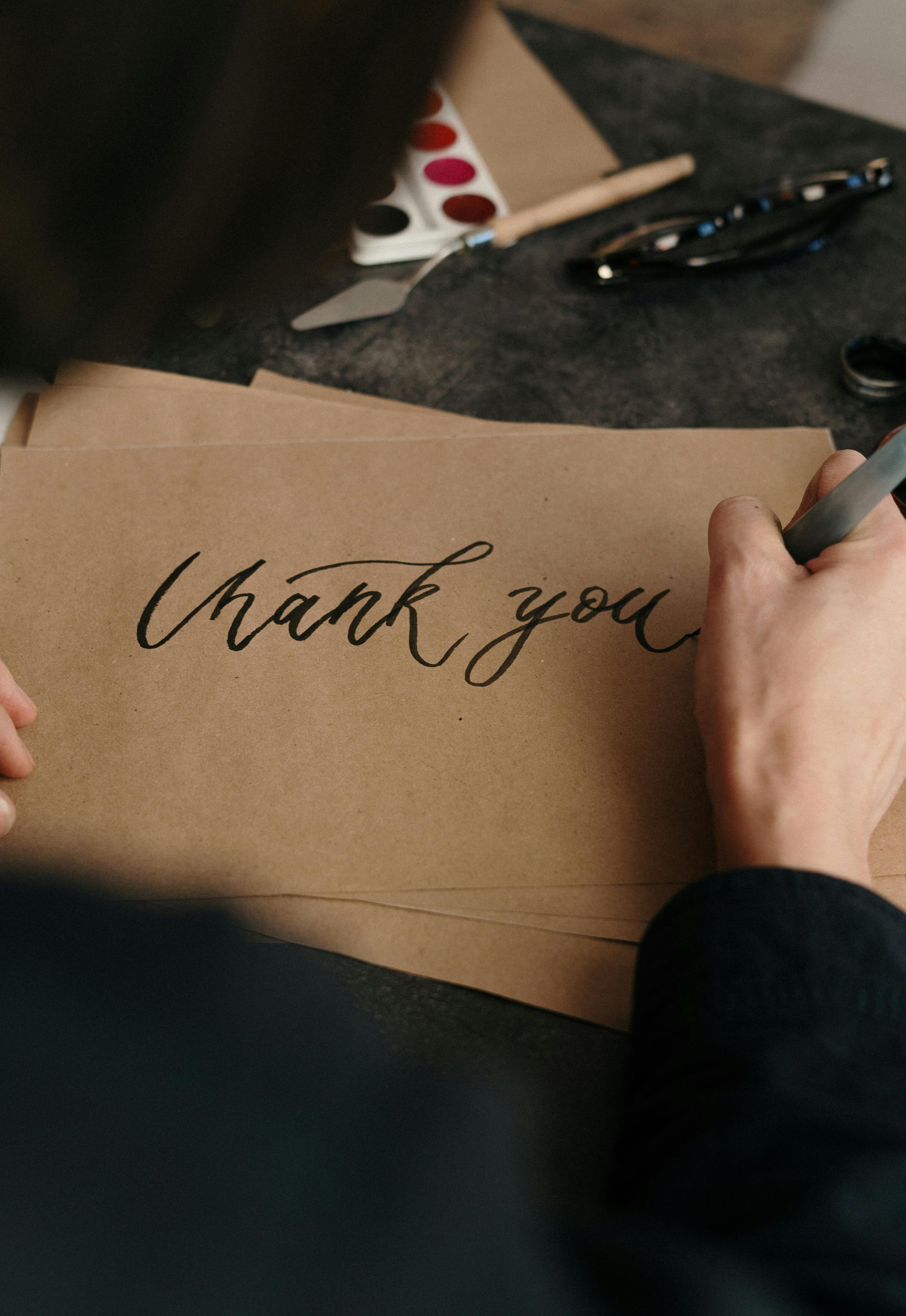 A person is writing a thank you note on a piece of brown paper.