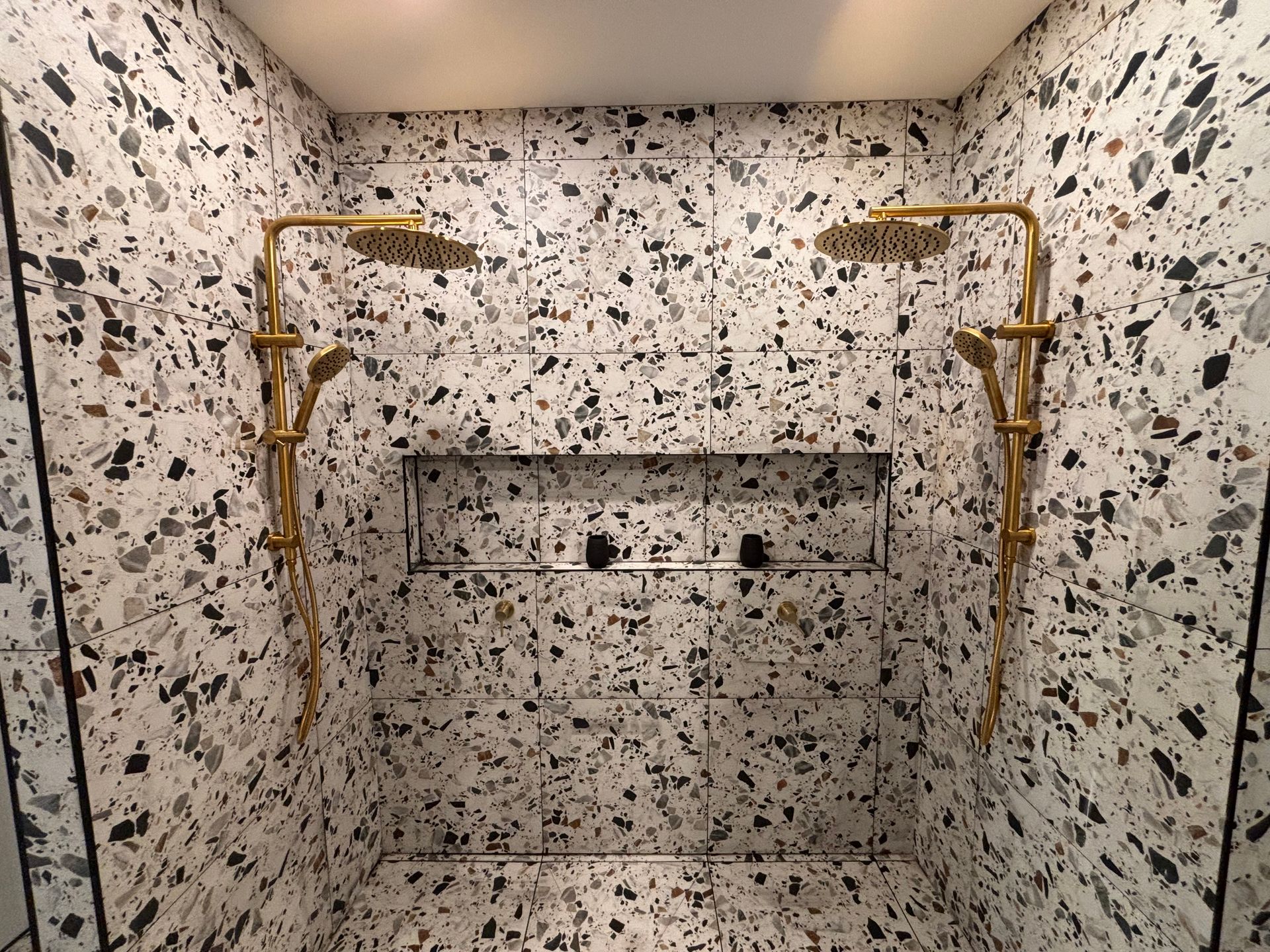 A bathroom with two shower heads and a terrazzo floor.