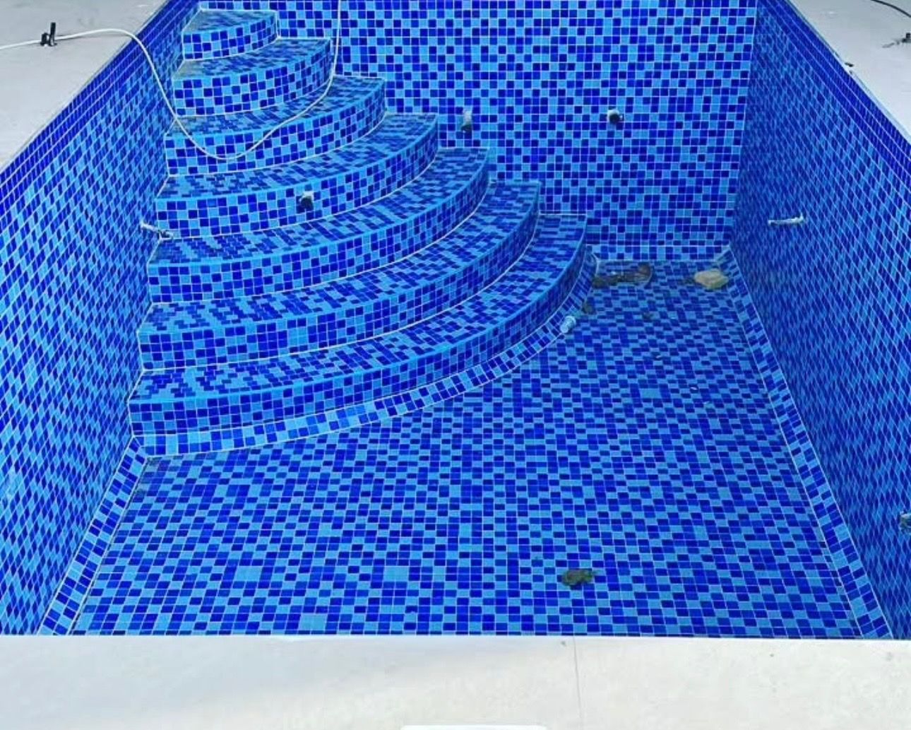A swimming pool with blue tiles and stairs is being built.