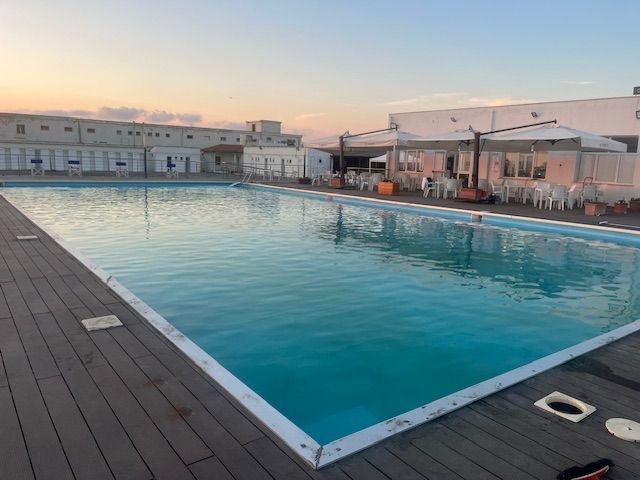 Piscina blu vuota con scale, scivolo e cielo azzurro.