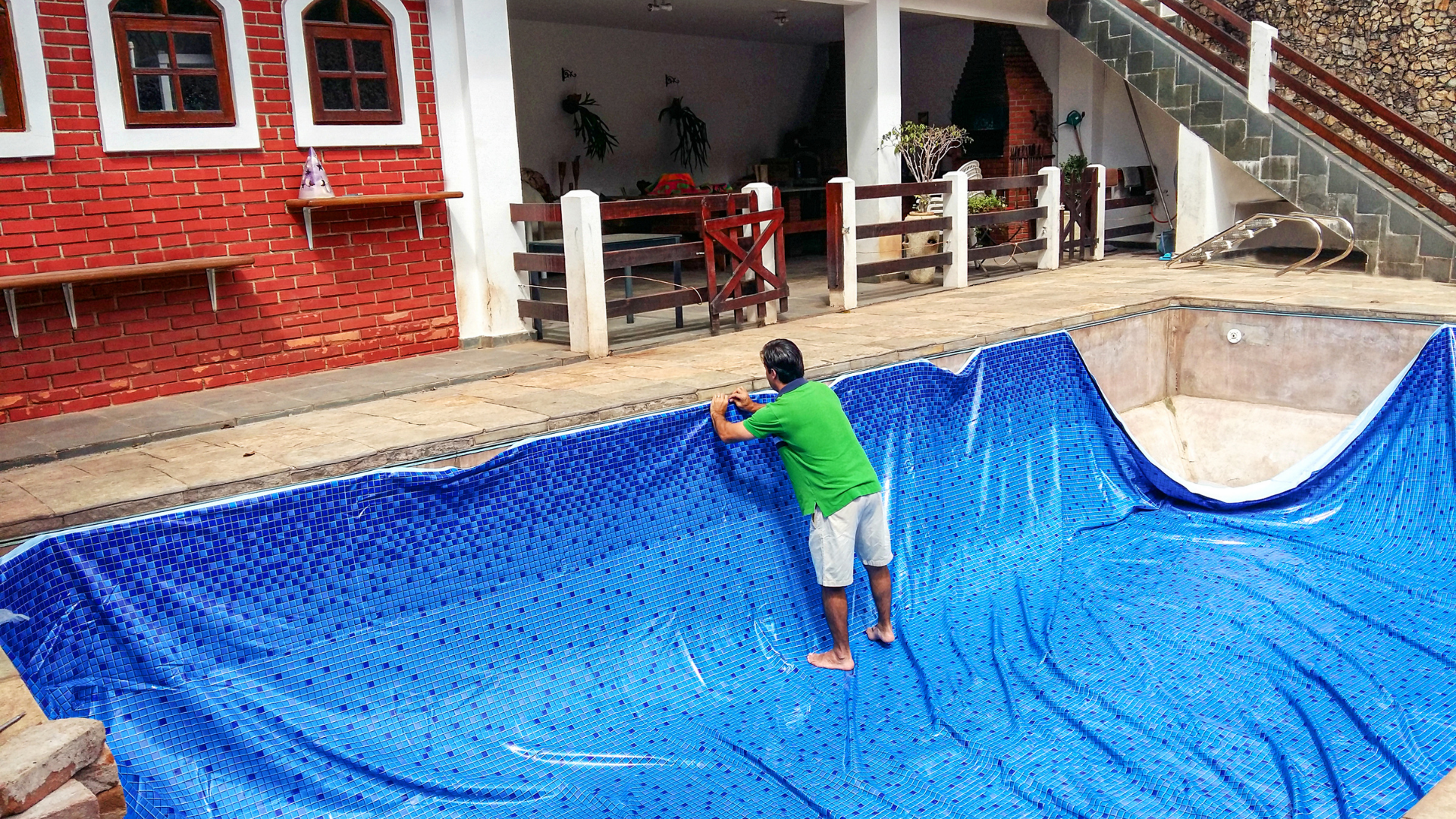 A man is covering a swimming pool with a blue tarp.