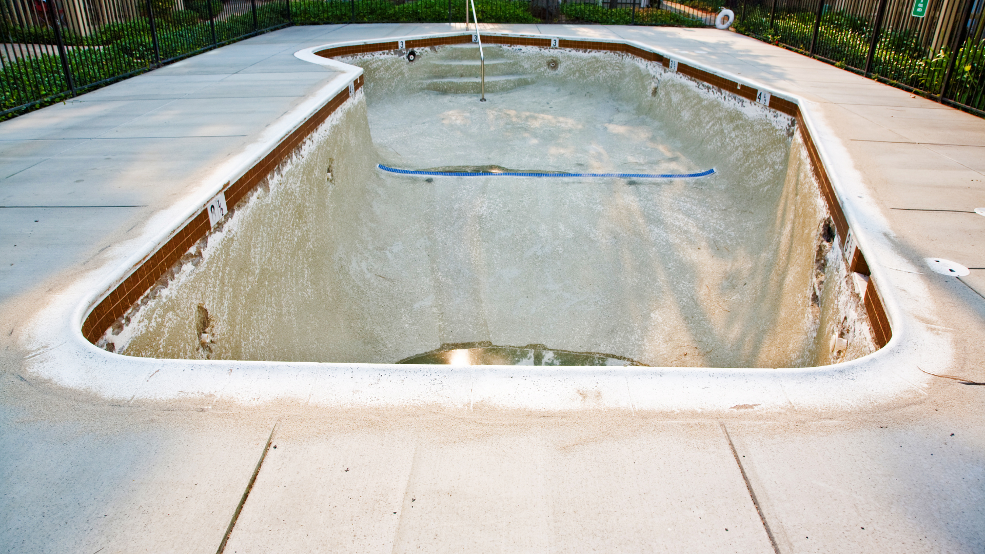 An empty swimming pool is sitting on a concrete deck.