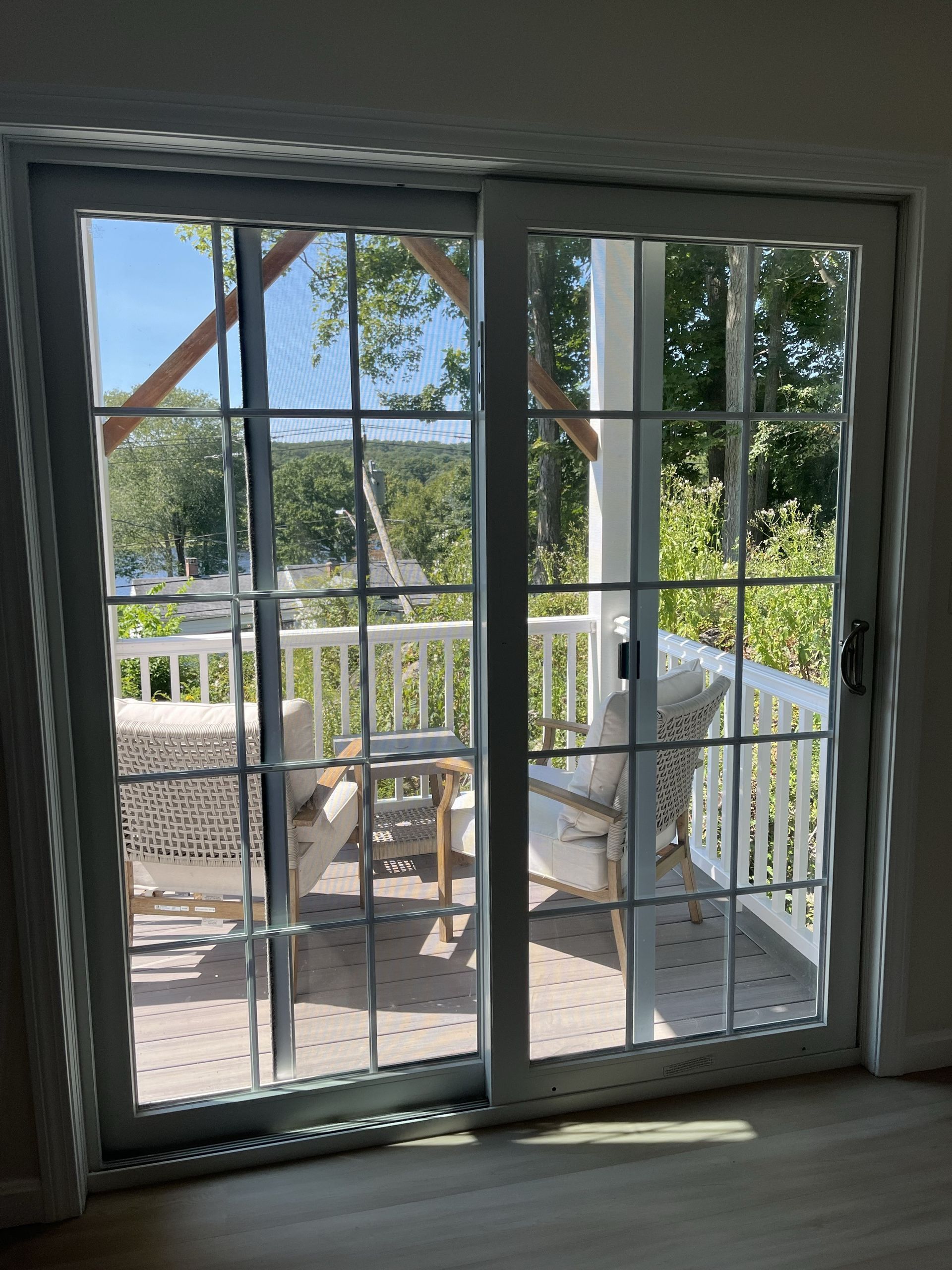 A sliding glass door with a grid pattern looking out onto a deck with two cushioned chairs and a table overlooking trees.