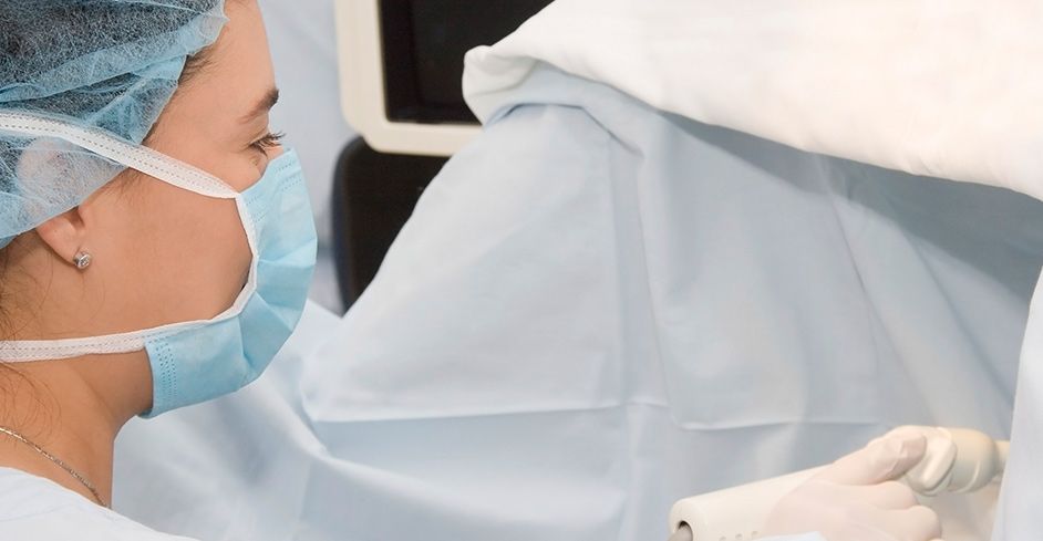 Cirujano con mascarilla y gorro durante una cirugía. Quirófano con campos quirúrgicos.