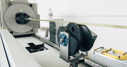 Macchina per pultrusione industriale che tira una barra composita attraverso una guida circolare e tra due rulli di tensionamento neri.