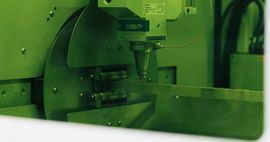 Un primo piano con tonalità verdastra mostra la testa di una macchina per il taglio laser intenta a eseguire un lavoro di precisione su un pezzo di metallo.