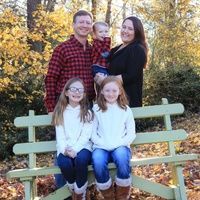 A family is sitting on a green bench in the woods.