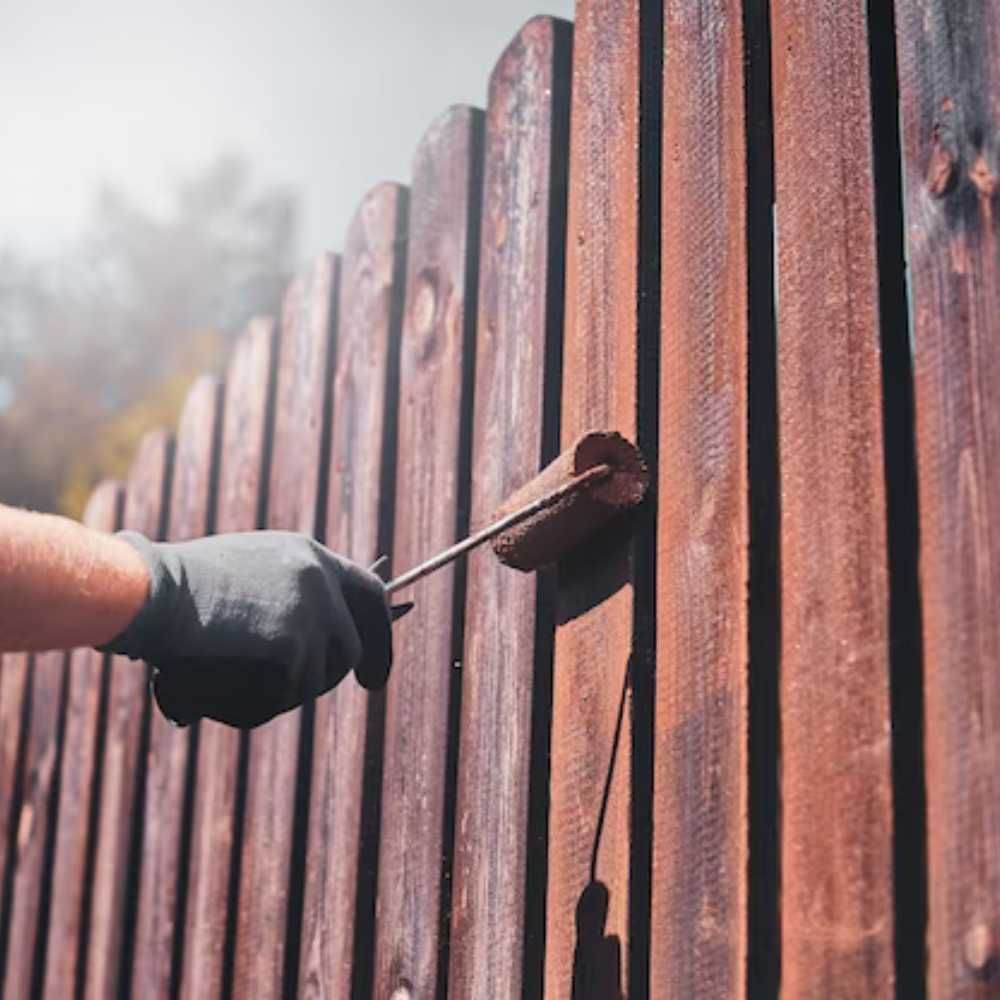 A person is painting a wooden fence with a roller.