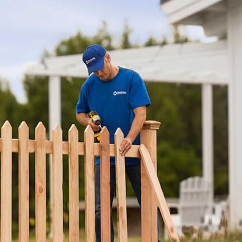 A man in a blue shirt is working on a wooden fence.