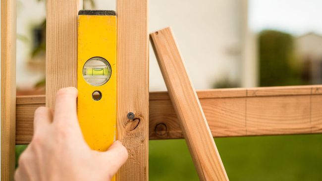 A person is measuring a piece of wood with a level.