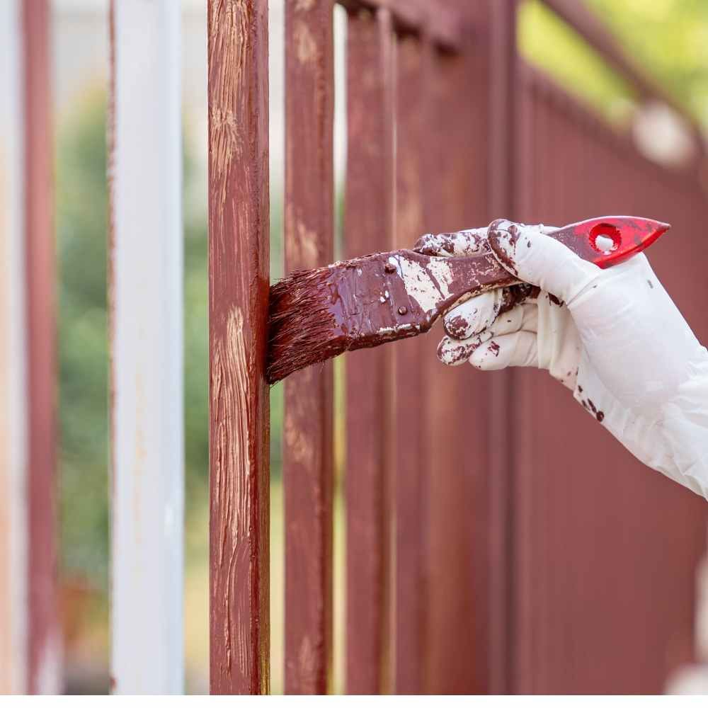 A person is painting a fence with a brush.