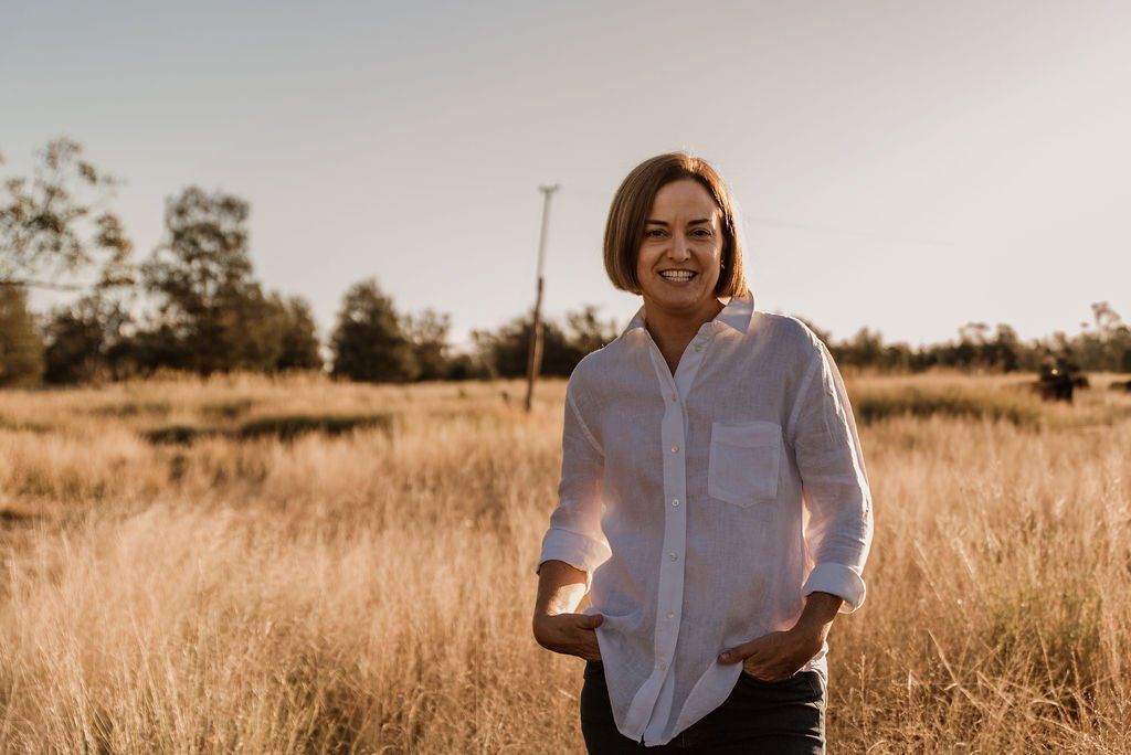 A woman in a white shirt is standing in a field of tall grass.