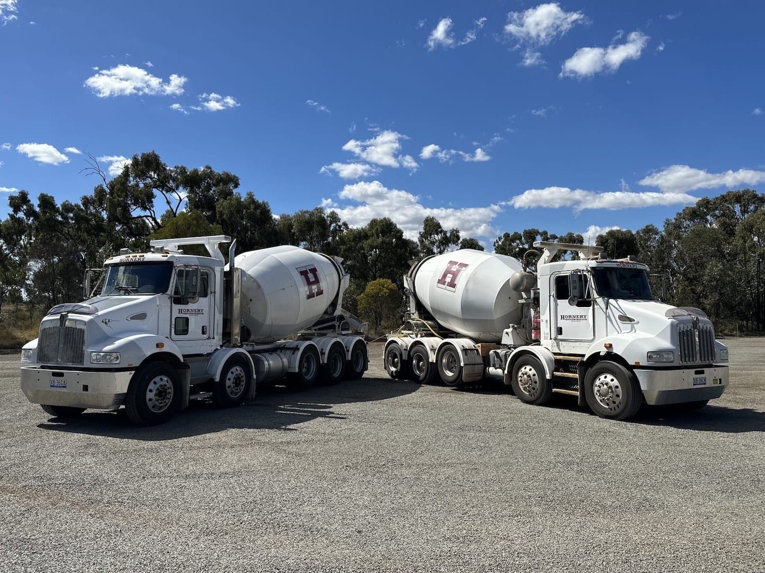 two concrete mixer trucks are parked next to each other in a gravel lot .