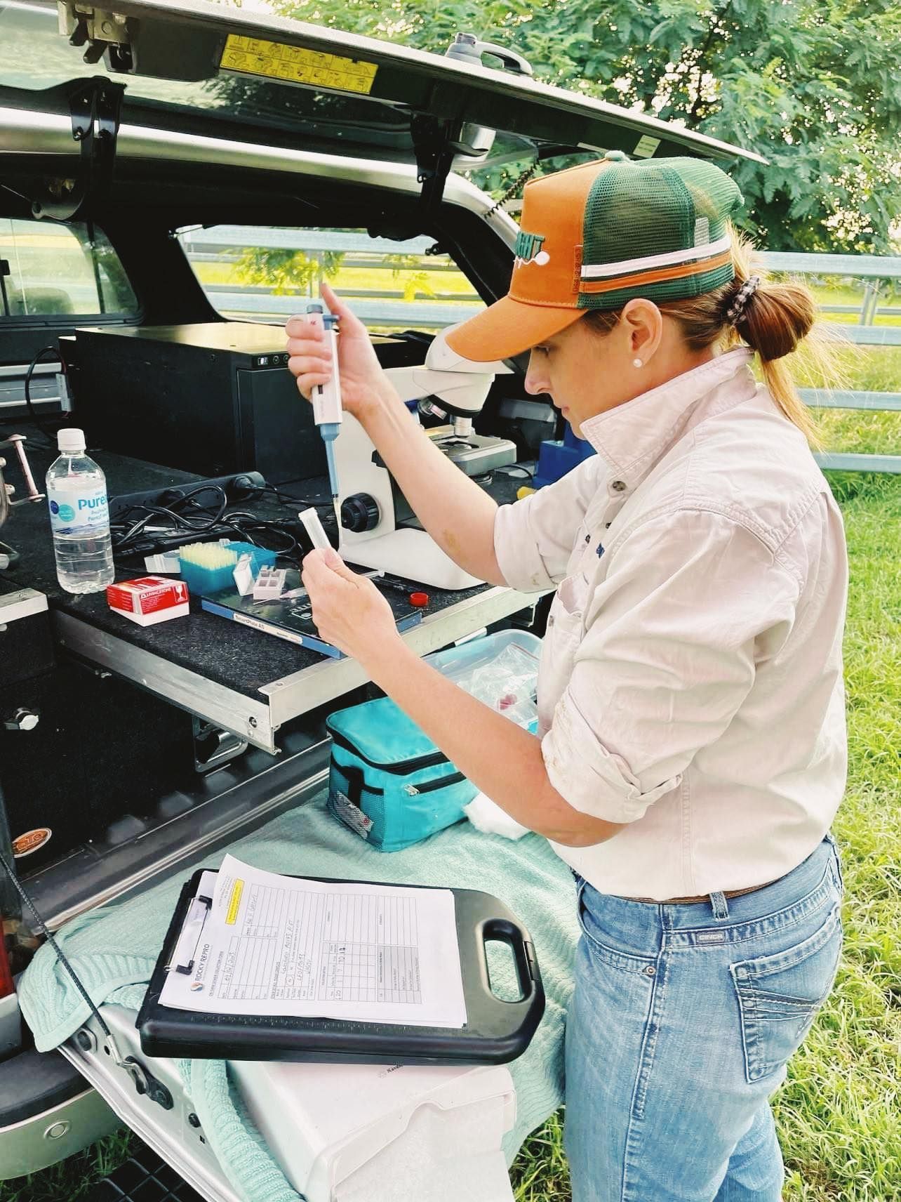 A woman is holding a pipette in front of a microscope.