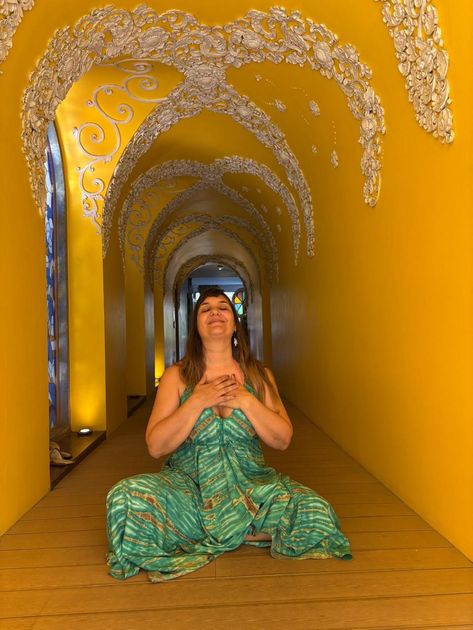 Mujer meditando en un túnel amarillo con intrincados diseños blancos, vestida con un vestido verde.