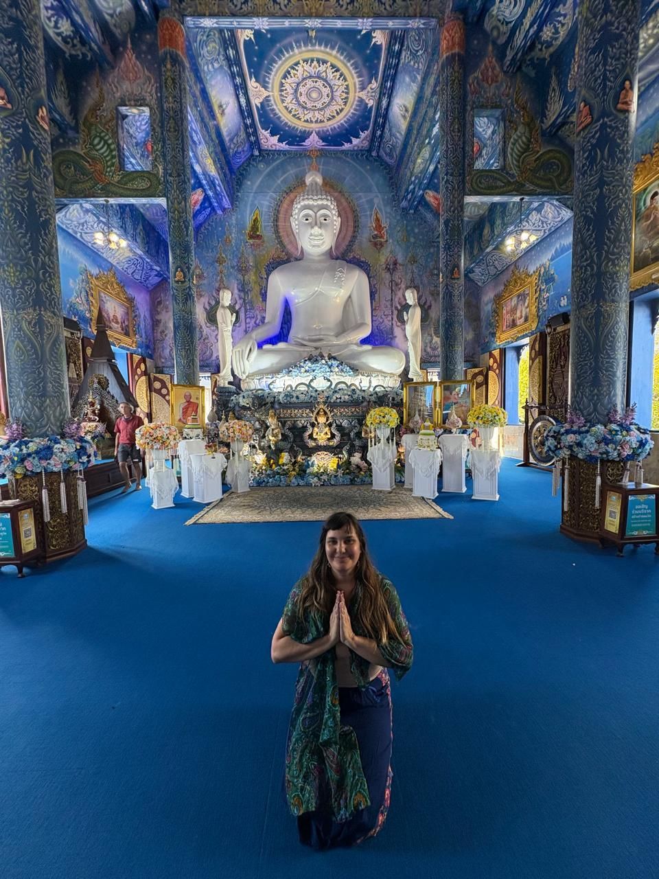 Persona de pie en el salón de un templo azul ornamentado, bajo una gran estatua de Buda.