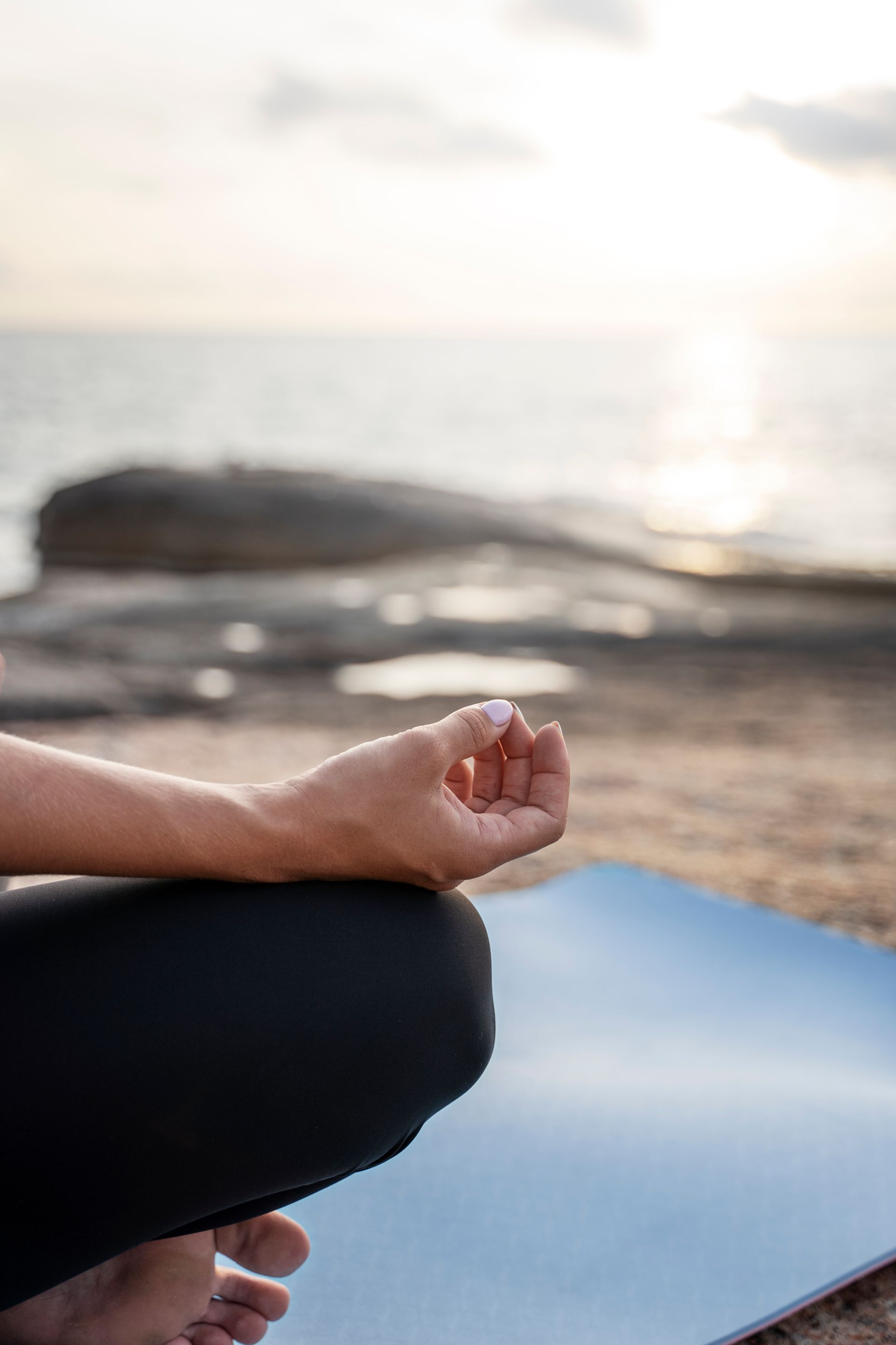 Persona meditando sobre una esterilla en la playa al atardecer.