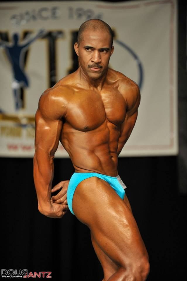 A bodybuilder poses in front of a sign that says ytd