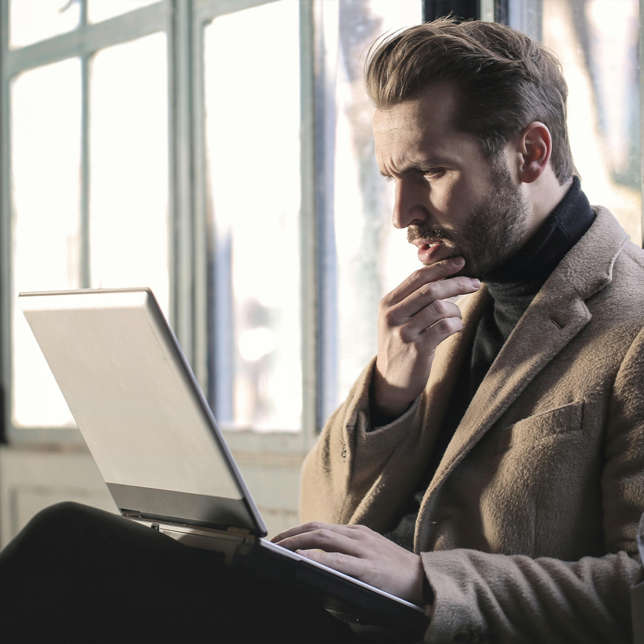 A person is typing on a laptop while holding a cell phone.