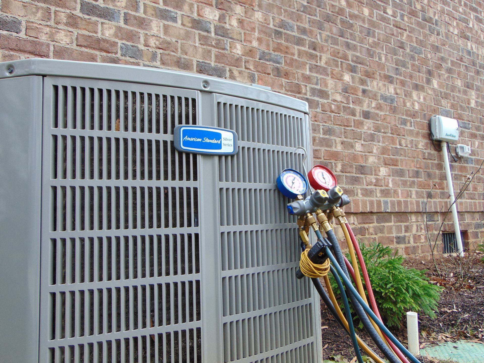 An air conditioner is being serviced outside of a brick building.