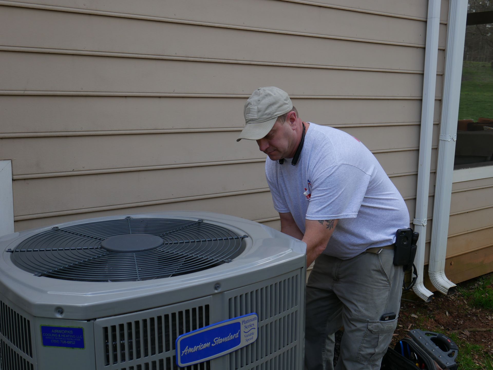A man is working on an air conditioner outside of a house
